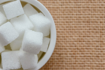 Purified sugar cubes on white bowl in top view flat lay with copy space for background or wallpaper. Seasoning for add to coffee or tea to sweet taste. Unhealthy or not good for diet and diabetes.