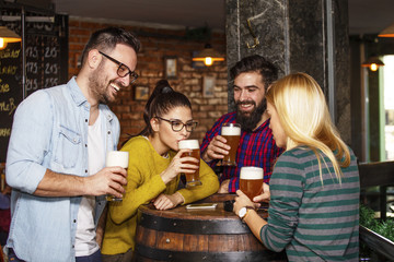 Group of four friends drinking beer in pub
