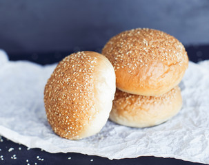 Three fresh buns on the butter-paper on the black background