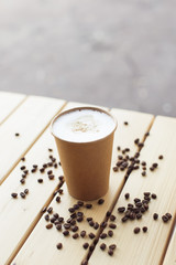 Cappuccino in brown paper cup with coffee beans on the table outdoor