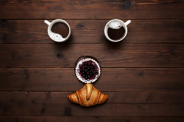 face of two cups of croissant and berry cake on wooden background