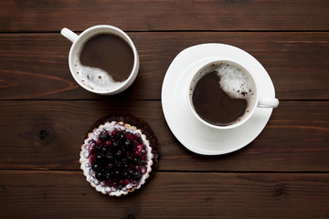 two cups of coffee and a berry cake on a wooden background