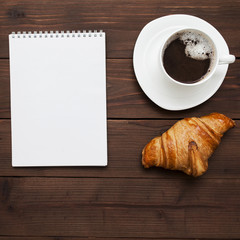 Obraz na płótnie Canvas notebook, coffee and croissant on a wooden background