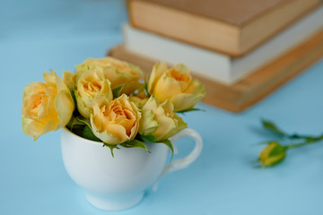yellow roses in a cup on a blue background, stack of books in the background