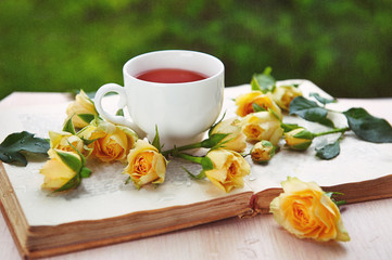 scattered yellow roses on an open book, a cup of tea, a natural background of nature
