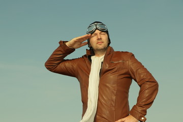 
Portrait of a vintage pilot with leather cap, scarf and aviator glasses salutes - Portrait of a...