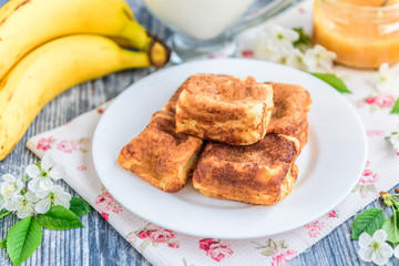 Cottage cheese pancakes in the form of cubes with banana, yogurt, honey and cherry blossom flowers on grey wooden background. Healthy breakfast food.