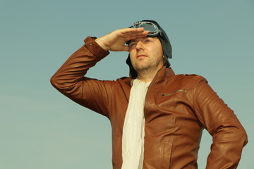 Portrait of a vintage pilot with leather cap, scarf and aviator glasses looks into the distance - Portrait of a man in historical pilot clothing
