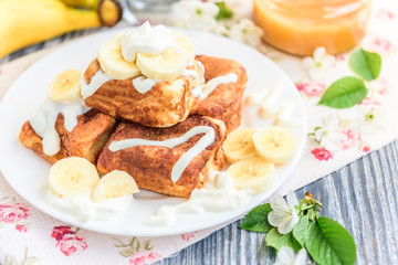 Cottage cheese pancakes in the form of cubes with banana, yogurt, honey and cherry blossom flowers on grey wooden background. Healthy breakfast food.