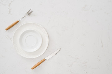 Eating concept. Spoon, fork and white dish on white stone background.