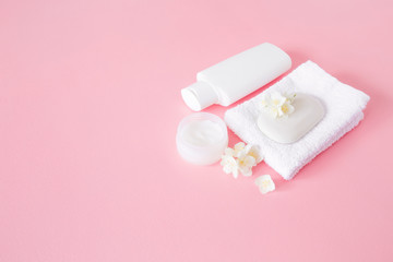 Obraz na płótnie Canvas White bottle, jar of natural herbal cream and soap for women on pastel pink background. Care about clean and soft face, hands, legs and body skin. Beautiful jasmine blossoms. Fresh flowers.