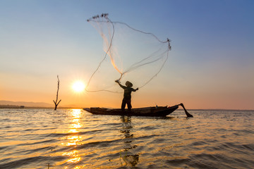 The silhouette of fisherman is throwing fishing nets to find the fish under lake in the morning.