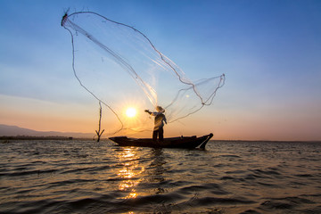 The silhouette of fisherman is throwing fishing nets to find the fish under lake in the morning.