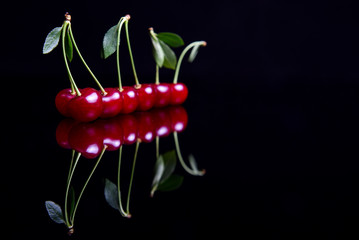 Symmetric reflection of red sour cherry on a black reflective surface © Toshe
