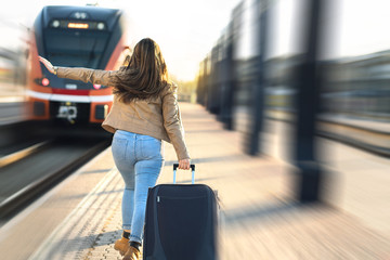 Late from train. Woman running and chasing the leaving train in station. Waving hand and rushing to get on. Female tourist with stress pulling suitcase in platform. © terovesalainen