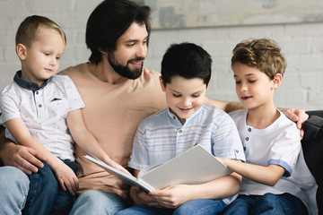 portrait of father and sons reading book together at home