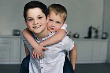 portrait of happy brothers piggybacking together at home