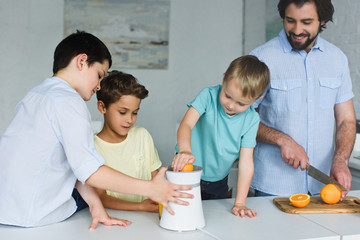 portrait of father and sons making fresh orange juice in kitchen at home