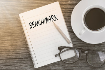 Benchmark concept on notebook with glasses, pencil and coffee cup on wooden table. Business concept.