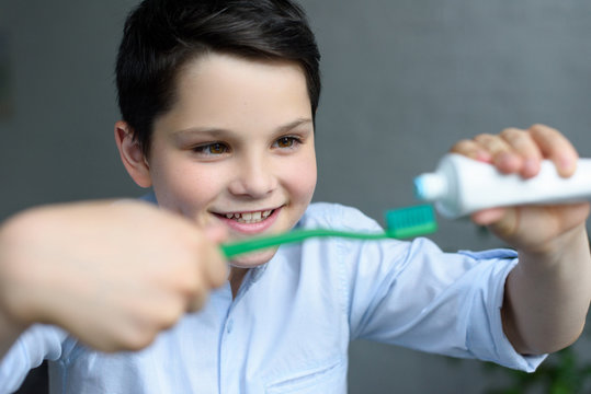 selective focus of little boy putting tooth paste on tooth brush in hand at home