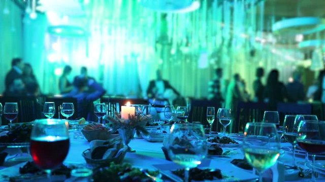 Banquet table in a restaurant with glasses and a candle. People dance against the background of the table. Banquet table, people dancing on the background