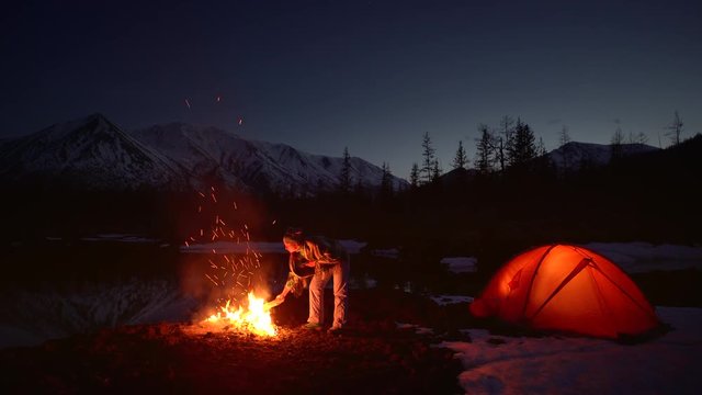 woman warming up in a camping by the fire in mountains