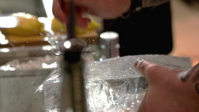 Barman breaking ice. Close up male hands splitting ice using sharp tool, slow motion.