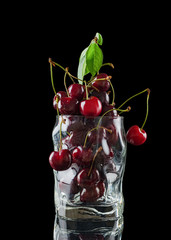 A bunch of fresh red cherries in a glass, isolated on a black background with a reflection on the ground.