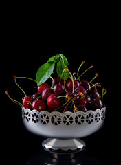 Fresh red cherries in vintage silver vase isolated on a black background with a reflection on the ground.