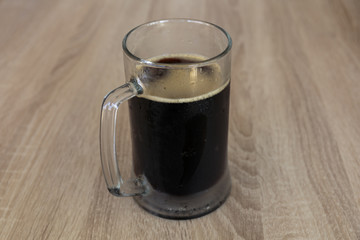 The damp mug of a cool dark beer on a wooden table in the pub.