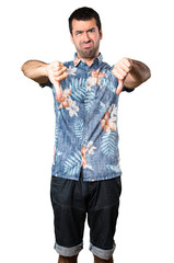 Handsome man with flower shirt making bad signal on isolated white background