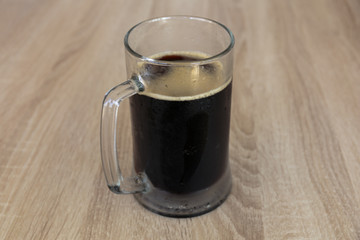 The damp mug of a cool dark beer on a wooden table in the pub.
