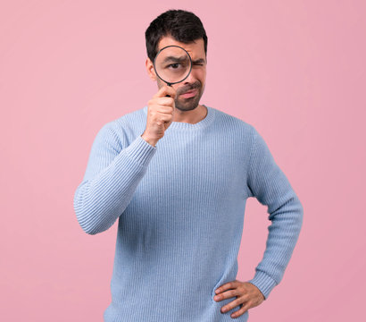 Man with blue sweater holding a magnifying glass on pink background