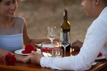 Affectionate Asian couple holding hands and chatting animatedly with each other while celebrating Saint Valentines Day on tropical beach at sunset
