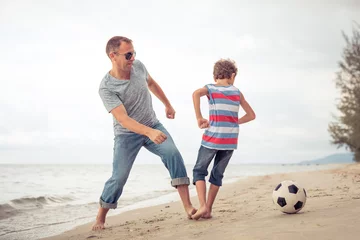 Fotobehang Father and son playing football on the beach at the day time. © altanaka
