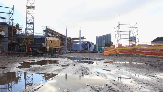 a low glide tracking shot of a wet construction site with rubble and cement mixer in the background.
