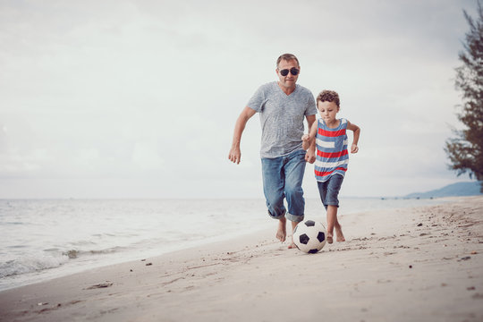 Father and son playing football on the beach at the day time.