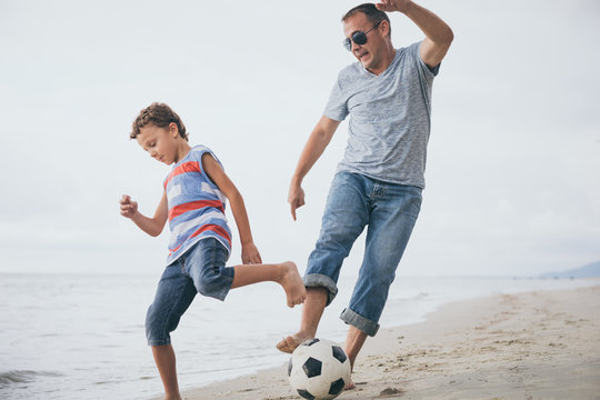 Father and son playing football on the beach at the day time.