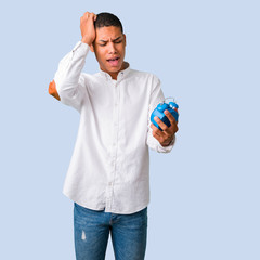 Young african american man with white shirt restless because it has become late and holding vintage alarm clock on isolated blue background