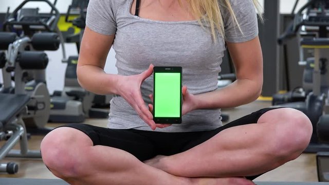 Closeup on a smartphone with a green screen a woman holds in a gym