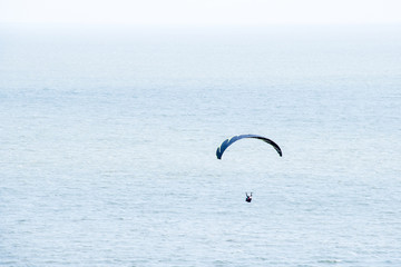 Unrecognizable paraglider flies against blue space of sky, sea