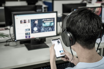 Student learning online study concept: Asian Younf man listening with Headphones and laptop, sitting holding smartphone chatting in home for e-learning in educational technology by self