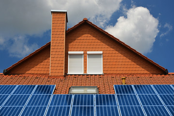 Photovoltaikanlage auf einem mit Kunststoff-Schindeln verkleideten Wohngebäude mit Schornstein, Dachfenster und Außen-Rollladen und Ziegeldach
