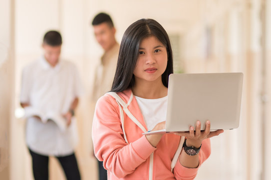 Online Education and E-learning Concept: Confident Asian Students Cute girl  using laptop computer for seaching, smiling at camera at Outside classroom at university with blur her friend background