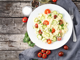 fresh diet vegetable salad with couscous, tomatoes, cucumbers, parsley, dark rustic wooden table, top view, copy space
