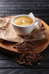 Hot cup of coffee on wooden plate with coffee beans spilled on background