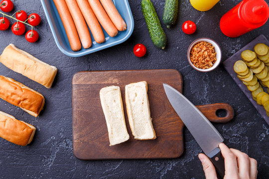Image on top of table with ingredients for hot dogs, cutting board, man's hands