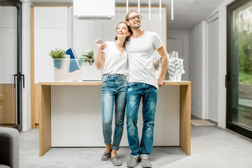Young and happy couple enjoying their new modern apartment standing at the kitchen with different home stuff on the background