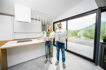 Young and happy couple holding boxes with different home stuff moving to a new modern house