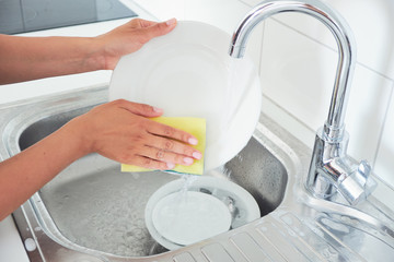 Cropped image of attractive young woman is washing dishes while doing cleaning at home